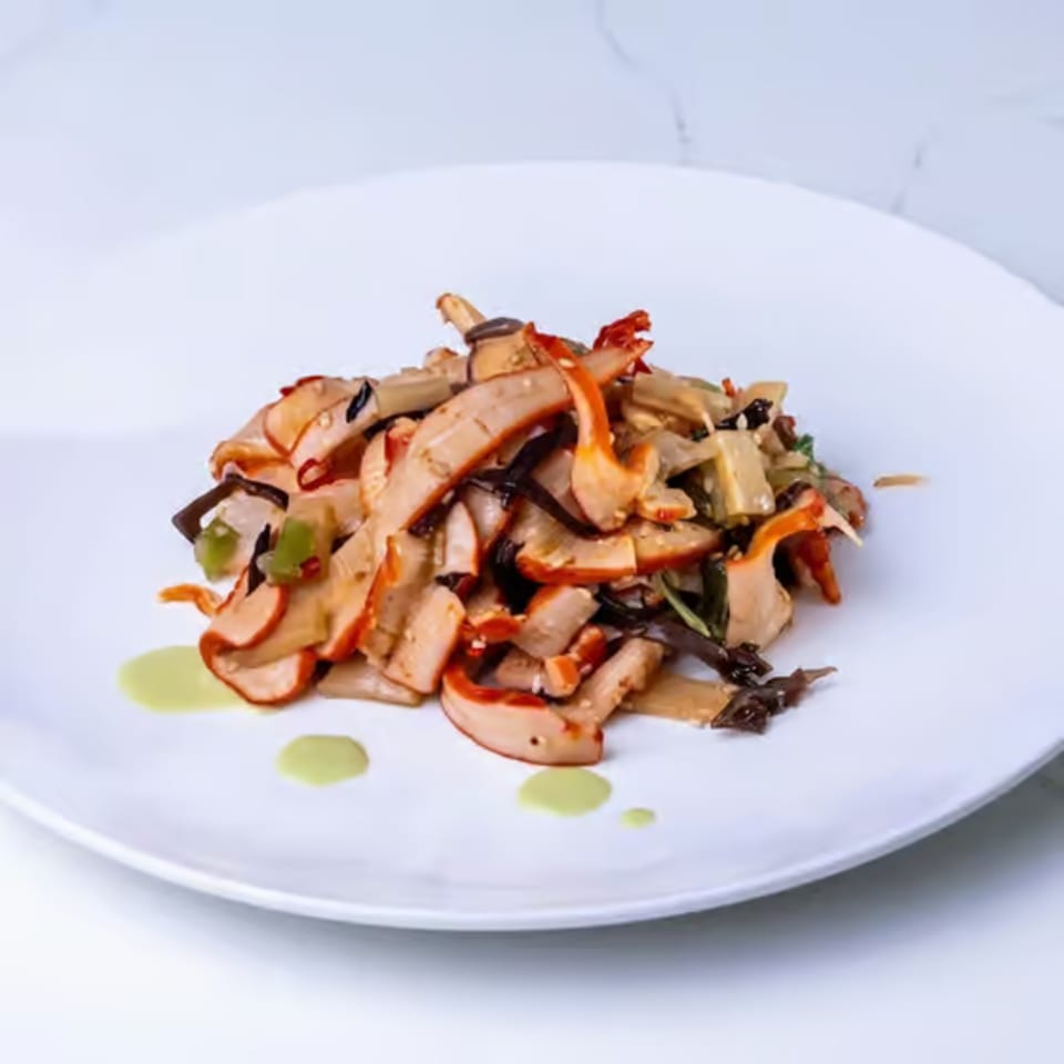 A white plate holds a colorful salad of sliced mushrooms, green peppers, and dark greens.