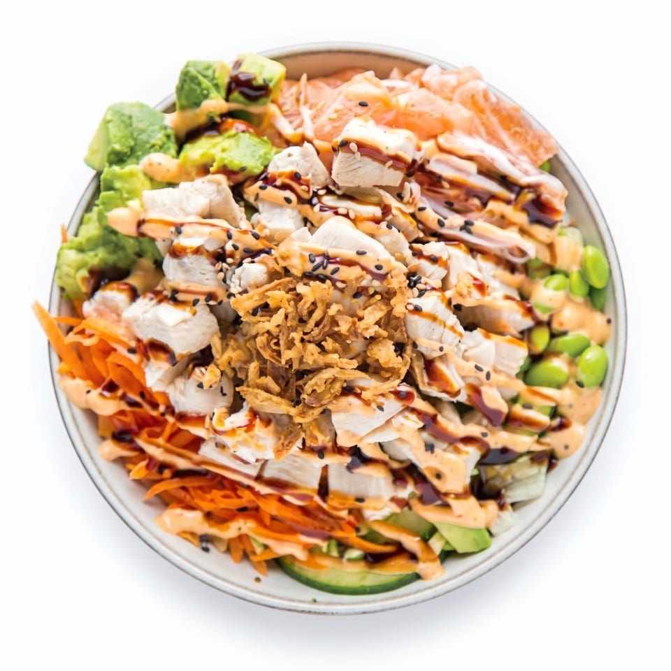 Overhead view of a colorful poke bowl with chicken, avocado, carrots, edamame, and crispy onions.