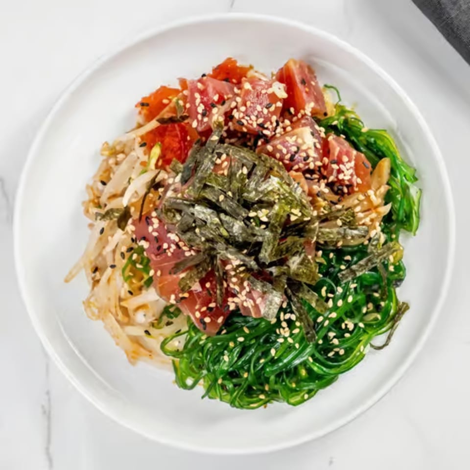 A vibrant poke bowl with tuna, seaweed, and other toppings, garnished with sesame seeds.