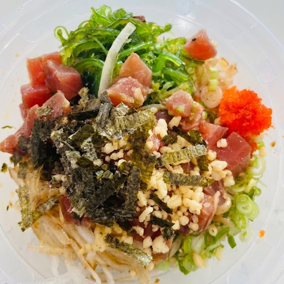 A vibrant poke bowl with tuna, seaweed, green onions, crispy bits, and orange roe.